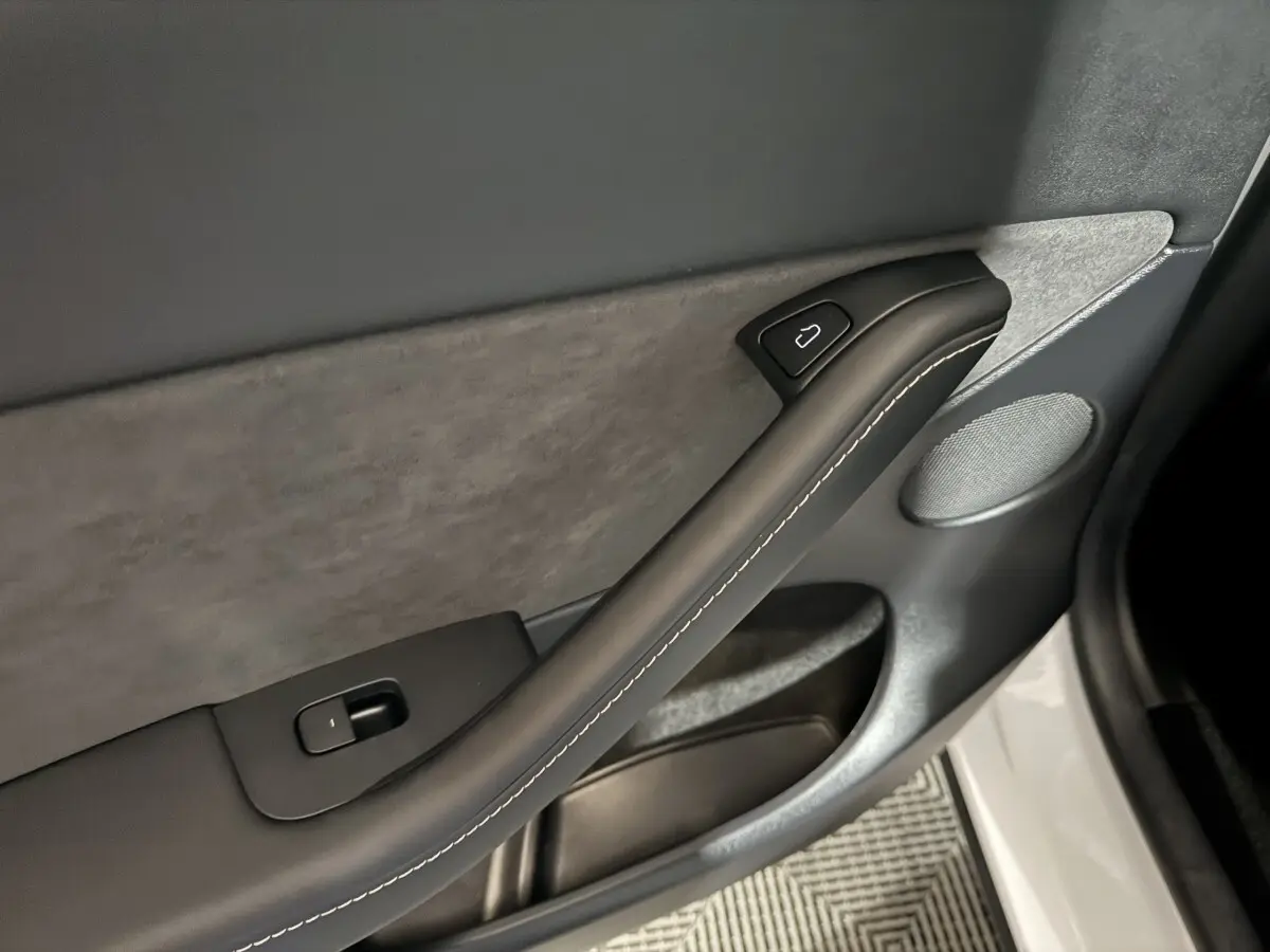 Détail de la porte intérieure côté conducteur d’une Tesla Model Y blanche, avec poignée noire et bouton de verrouillage.