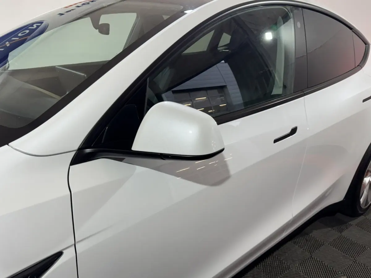 Vue côté gauche rapprochée du Tesla Model Y blanc, mettant en valeur la poignée affleurante et le rétroviseur électrique.