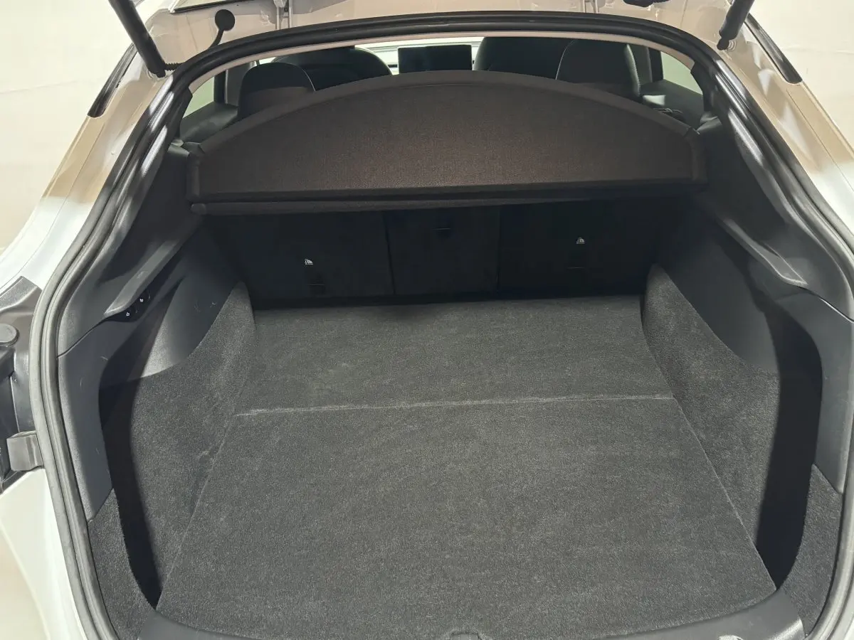 Coffre ouvert vu de l'arrière d'une Tesla Model Y blanc, espace de chargement spacieux et tapis noir.