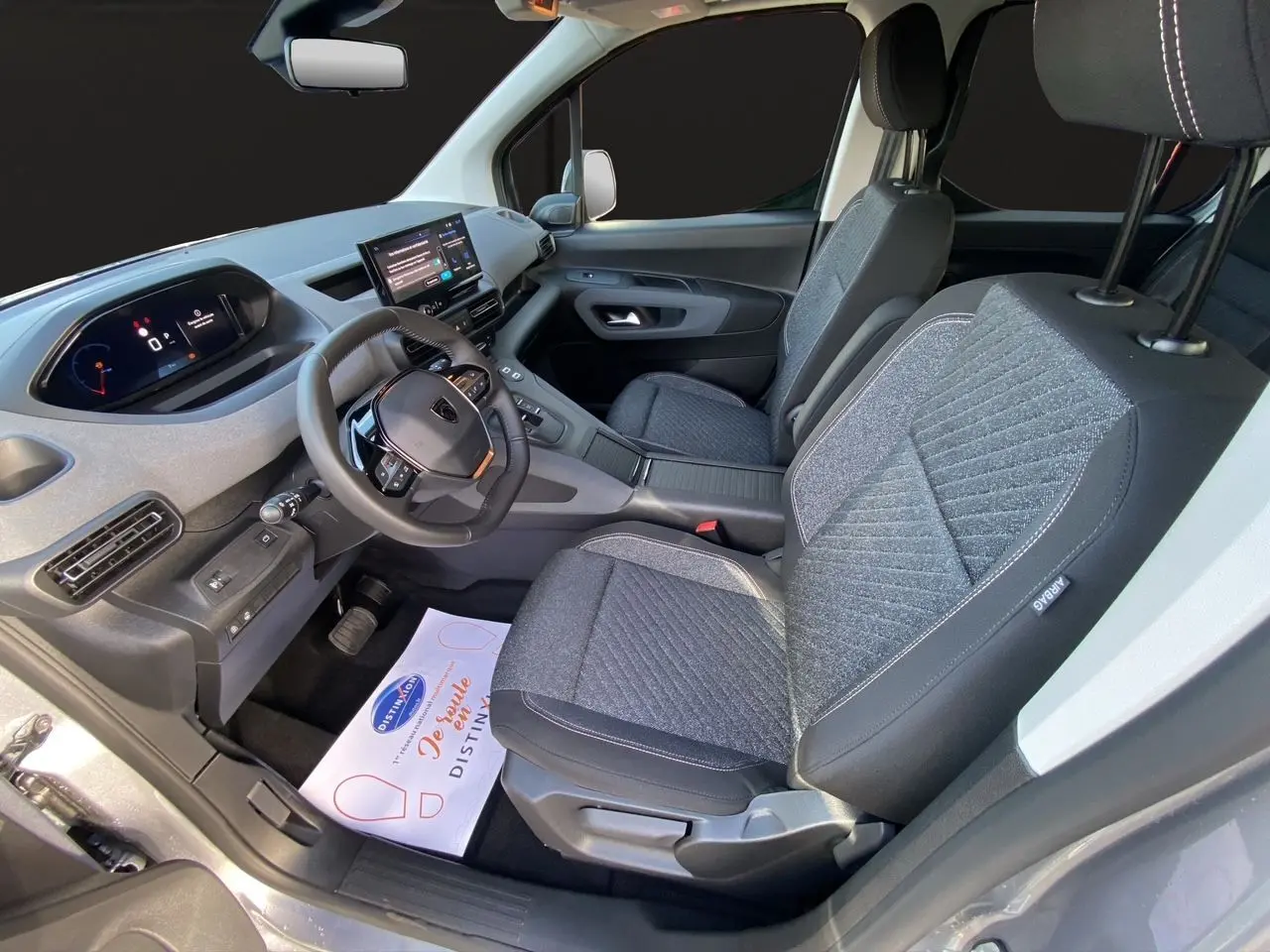 Vue intérieure côté conducteur du Peugeot Rifter gris acier 2026, avec sièges tissu et tableau de bord numérique.