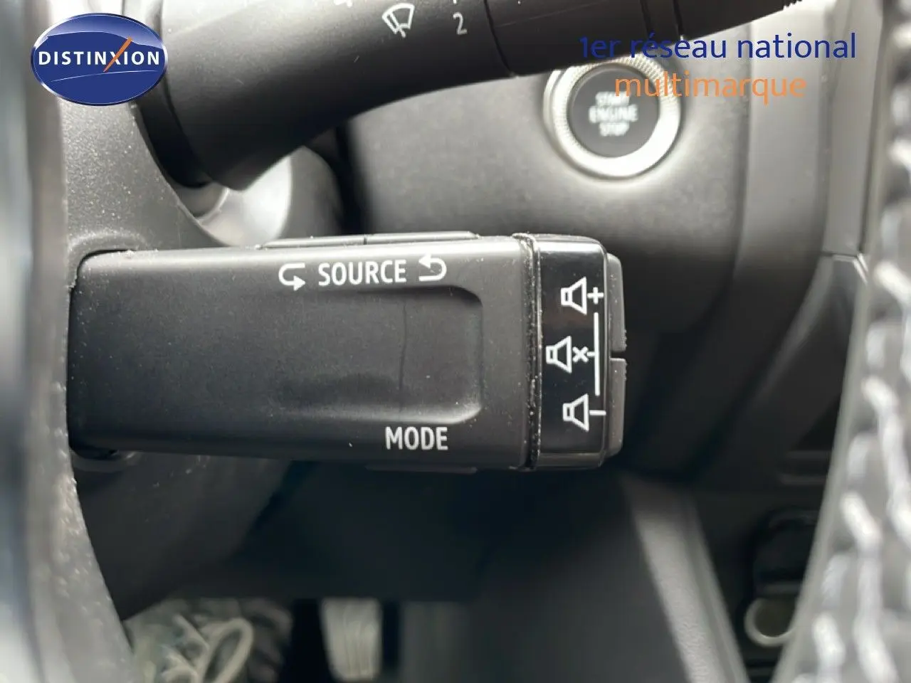 Gros plan sur la commande multimédia au volant du Renault Symbioz gris Rafale métal, avec bouton start visible en arrière-plan.