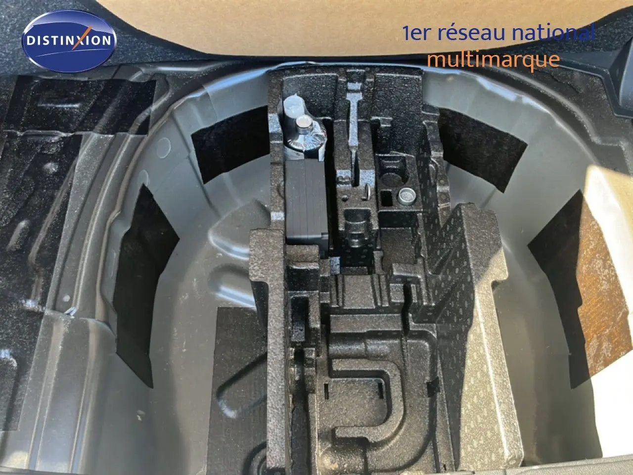 Vue plongeante sur le coffre ouvert d'une Skoda Fabia noire, montrant le rangement pour roue de secours et outils.
