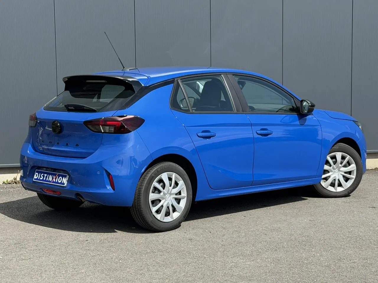Opel Corsa bleu Voltaic vue 3/4 arrière droit, avec feux arrière fumés et jantes blanches.