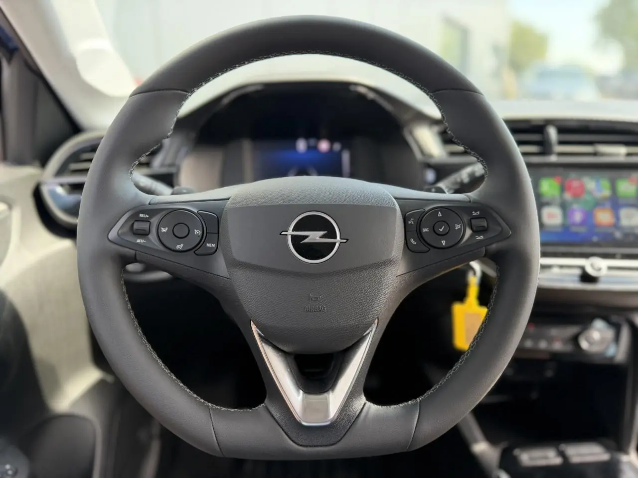 Vue rapprochée du volant en cuir noir de l’Opel Corsa 2025 avec commandes multifonctions et écran tactile en arrière-plan.