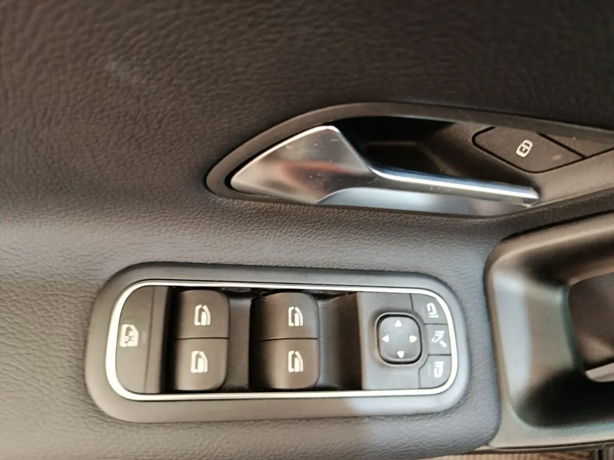 Gros plan sur la commande des vitres électriques et poignée intérieure en métal dans une Mercedes Classe A noire.
