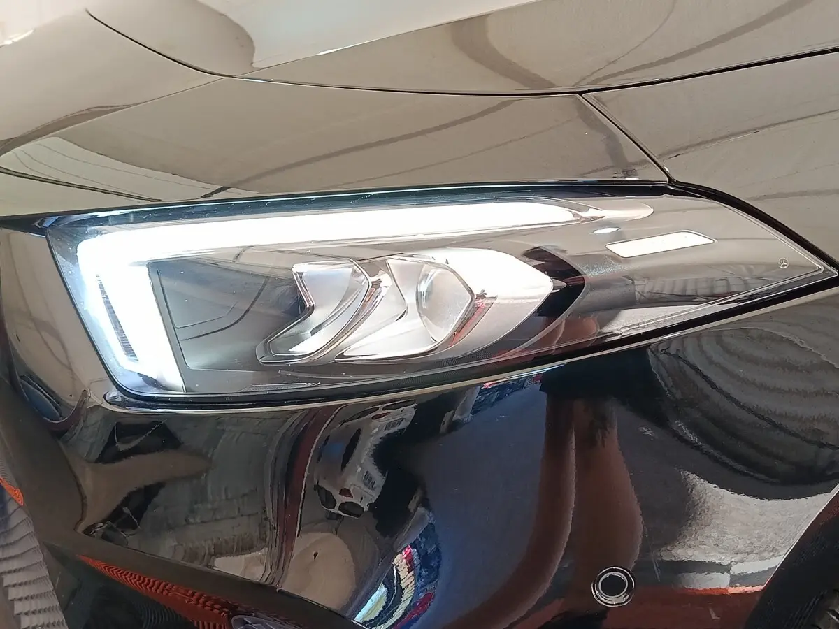 Gros plan sur le phare avant droit allumé d’une Mercedes Classe A 250 e Business Line noire, reflet brillant sur la carrosserie.