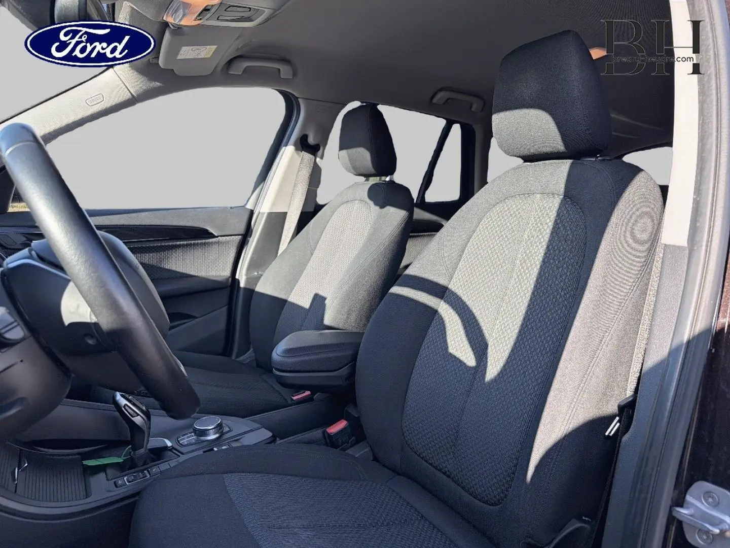 Vue intérieure avant droite du BMW X1 sDrive18dA 2018 avec sièges tissu noirs et accoudoir central.