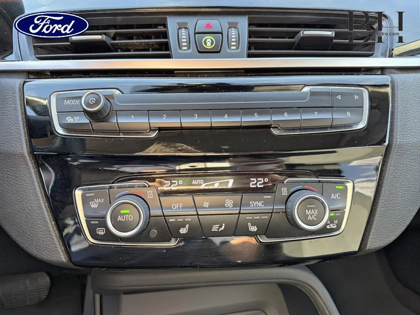 Tableau de bord noir brillant d'une BMW X1 sDrive18dA 2018, vue rapprochée sur la console de climatisation et audio.