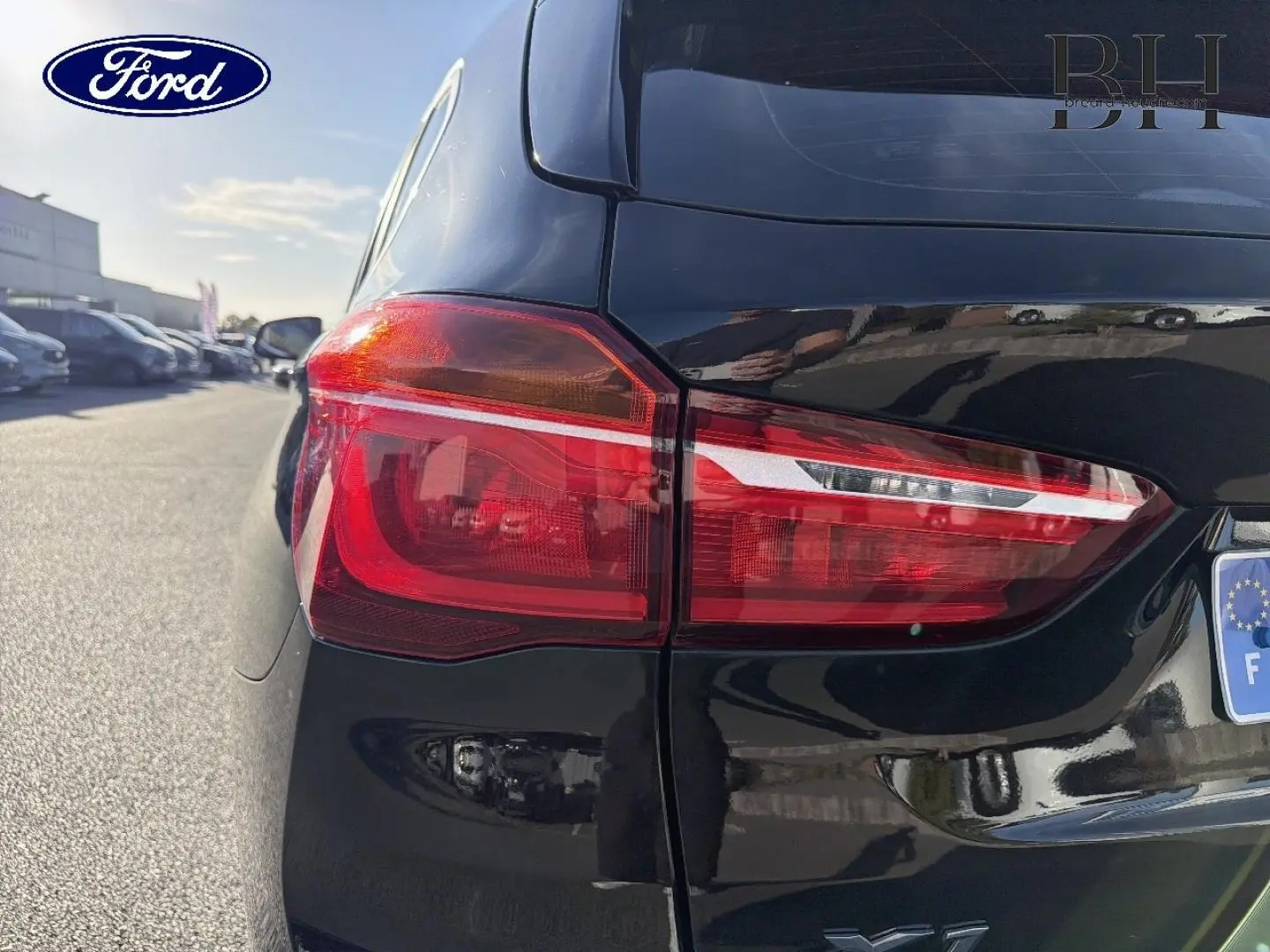 Gros plan sur le feu arrière gauche d’un BMW X1 sDrive18dA 2018 en noir Saphirschwarz, avec reflet sur la carrosserie brillante.