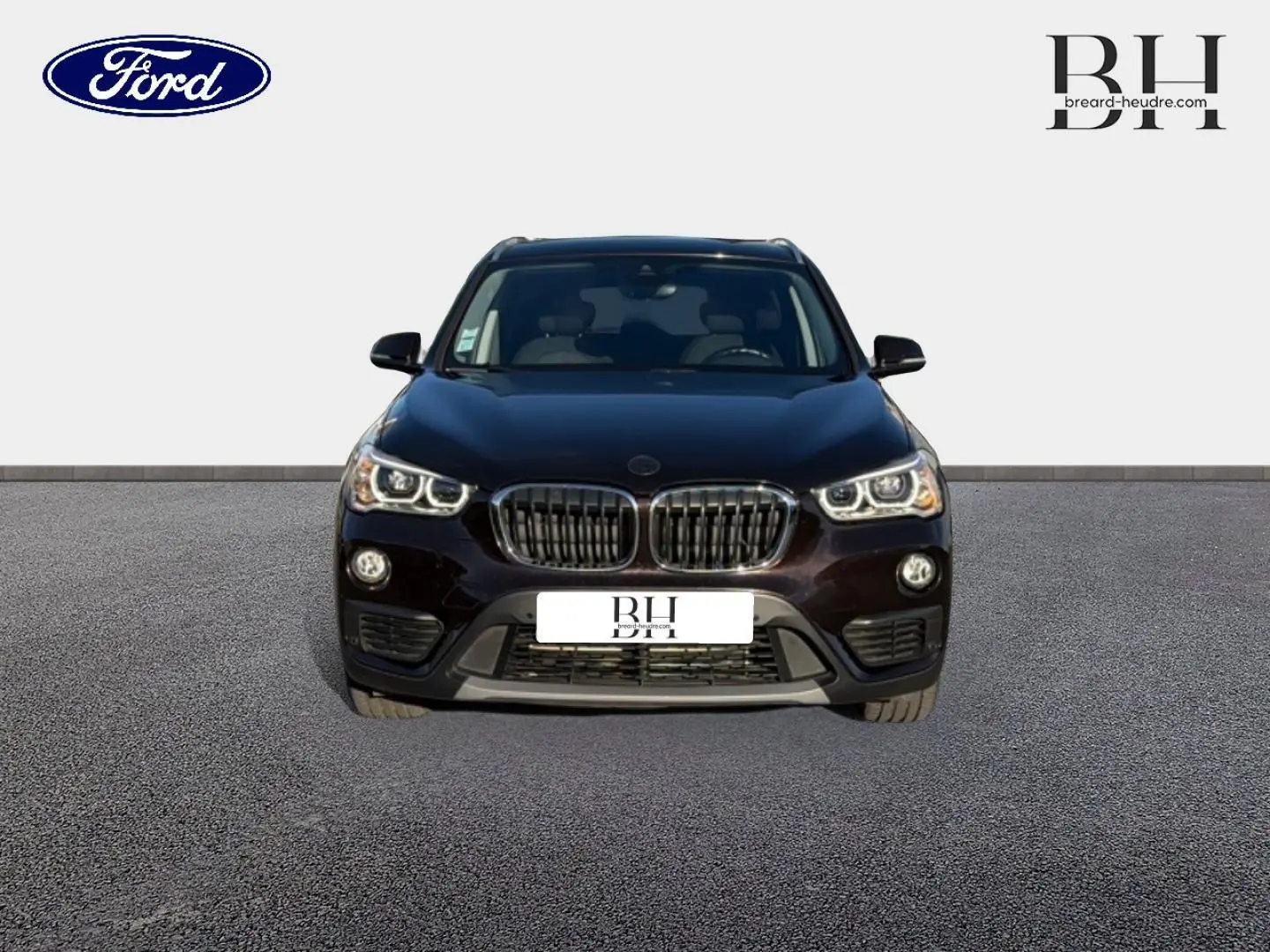 Vue de face d’un BMW X1 sDrive18dA 150ch Lounge noir Saphirschwarz avec calandre caractéristique et phares allumés.