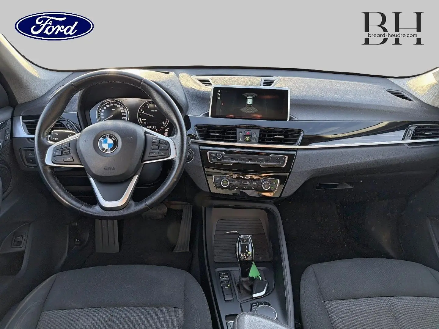 Vue intérieure avant de la BMW X1 sDrive18dA 2018 avec volant cuir multifonction et console centrale noire.