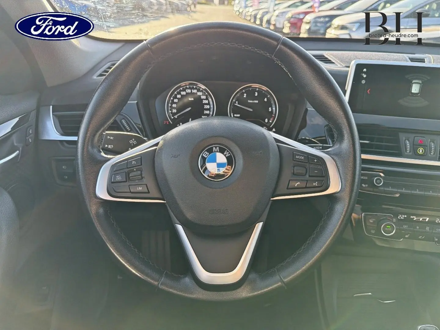 Vue intérieure centrée sur le volant cuir multifonction d'une BMW X1 noire avec tableau de bord et écran multifonction.