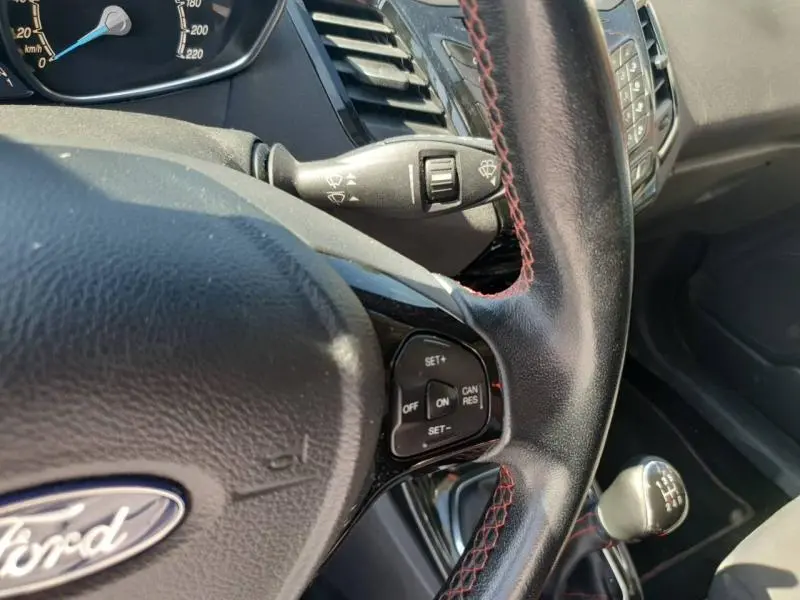 Gros plan sur le volant cuir noir avec surpiqûres rouges et levier de vitesse manuel dans une Ford Fiesta noire de 2015.