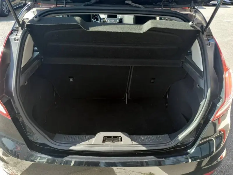 Coffre ouvert vu de l'arrière d'une Ford Fiesta noire, montrant l'espace de chargement et la tablette cache-bagages relevée.