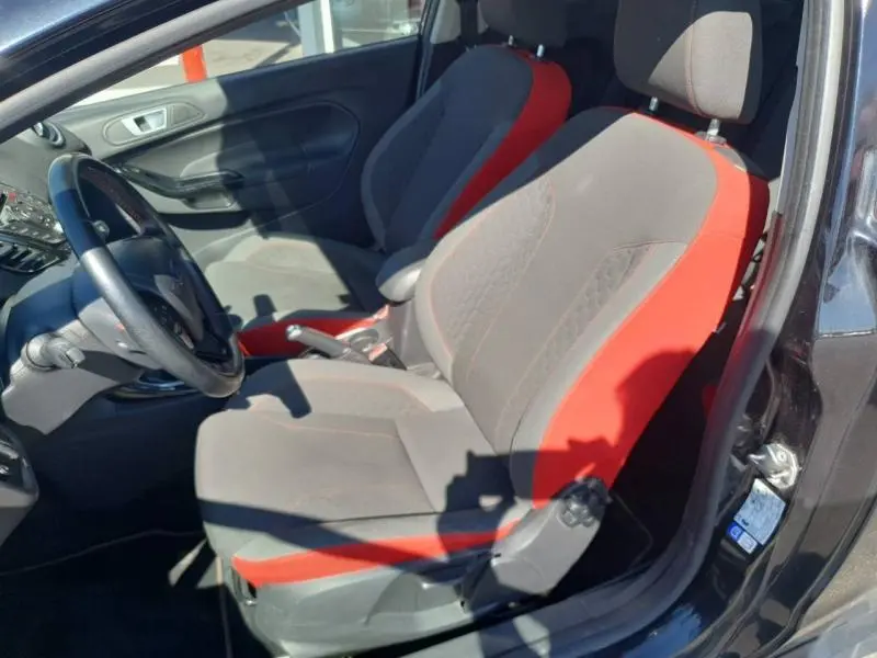 Vue intérieure côté conducteur de la Ford Fiesta noire, sièges sport gris et rouge avec volant cuir multifonction.