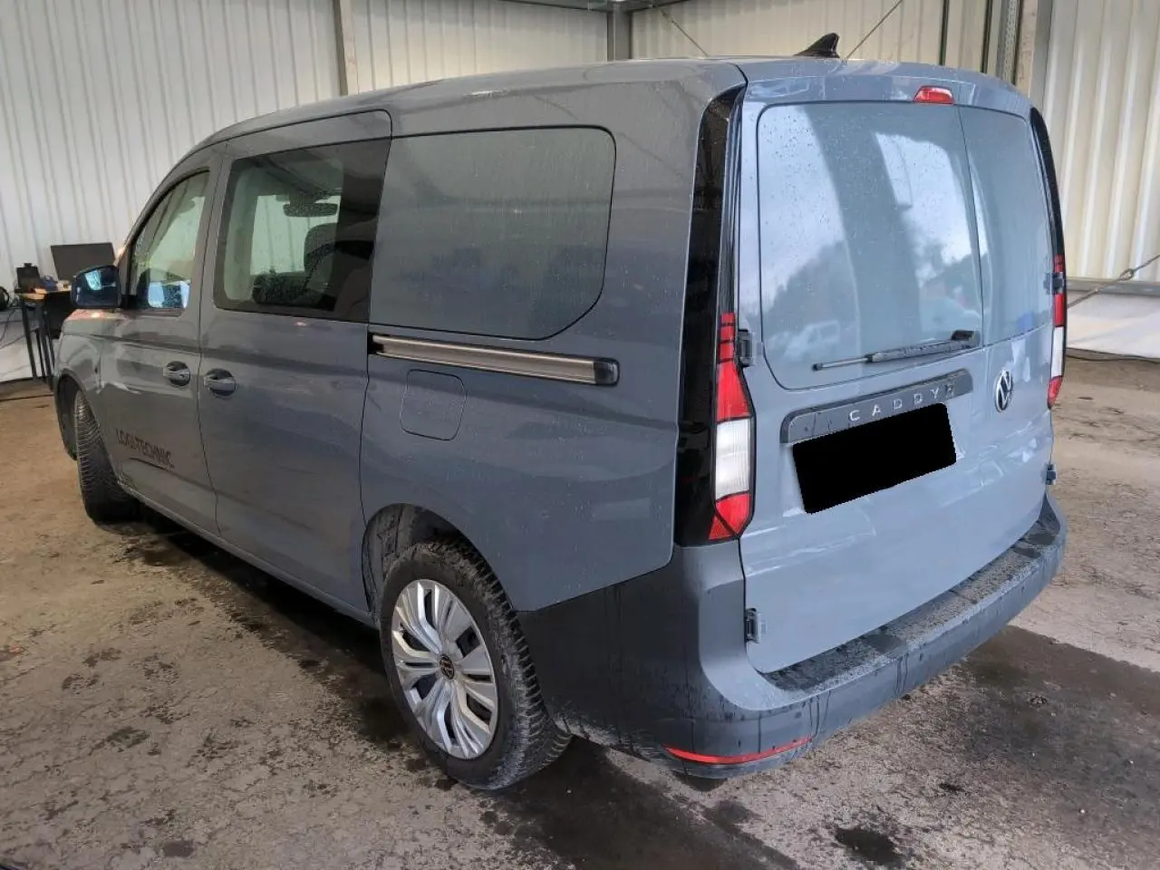 Vue 3/4 arrière droite d'un Volkswagen Caddy Maxi 2024 gris Pure Grey avec portes arrière battantes et vitres teintées.
