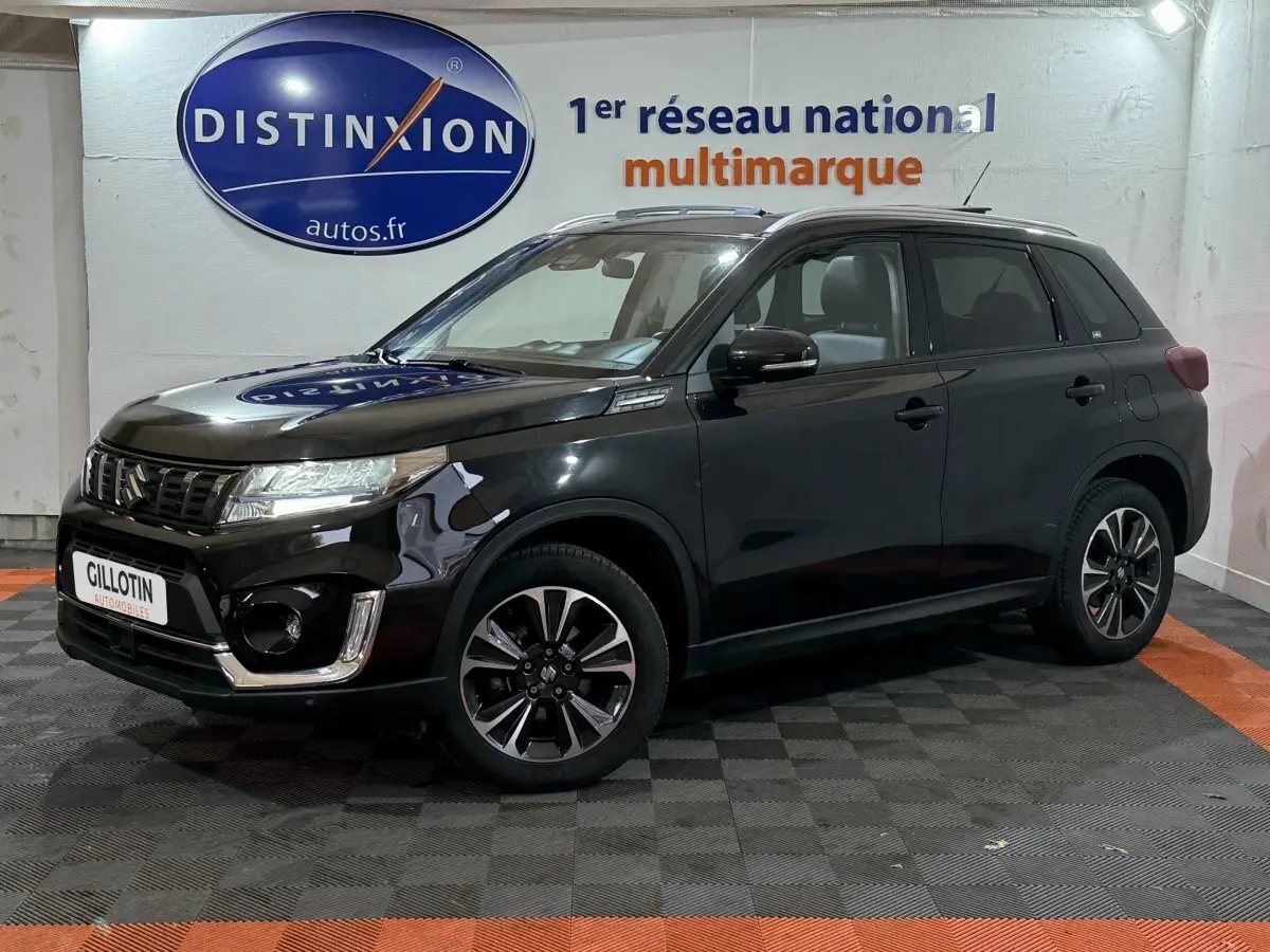 Suzuki Vitara noir en vue 3/4 avant droit, avec jantes alliage et calandre chromée brillante.
