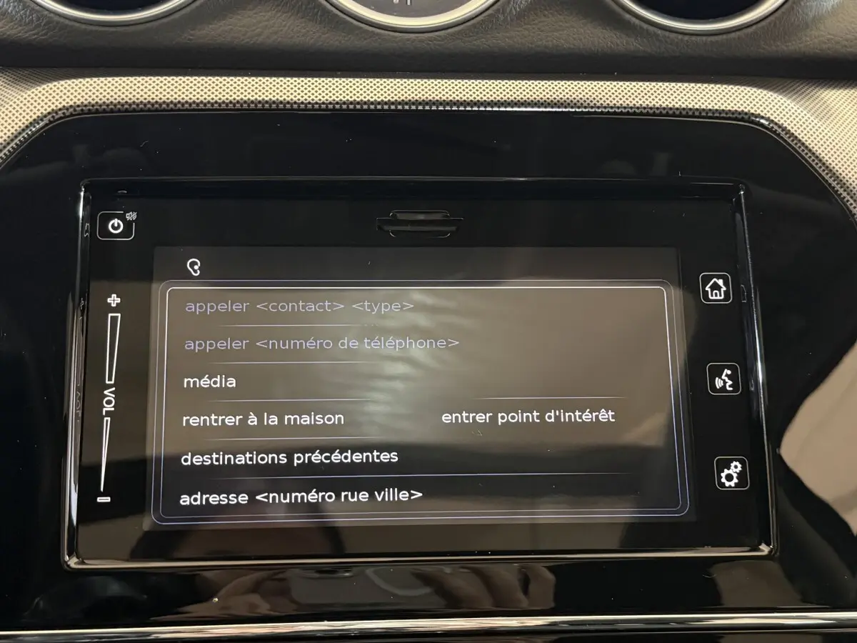 Écran tactile central du Suzuki Vitara 1.5 Dualjet hybrid STYLE 2022 affichant le menu vocal en intérieur noir.