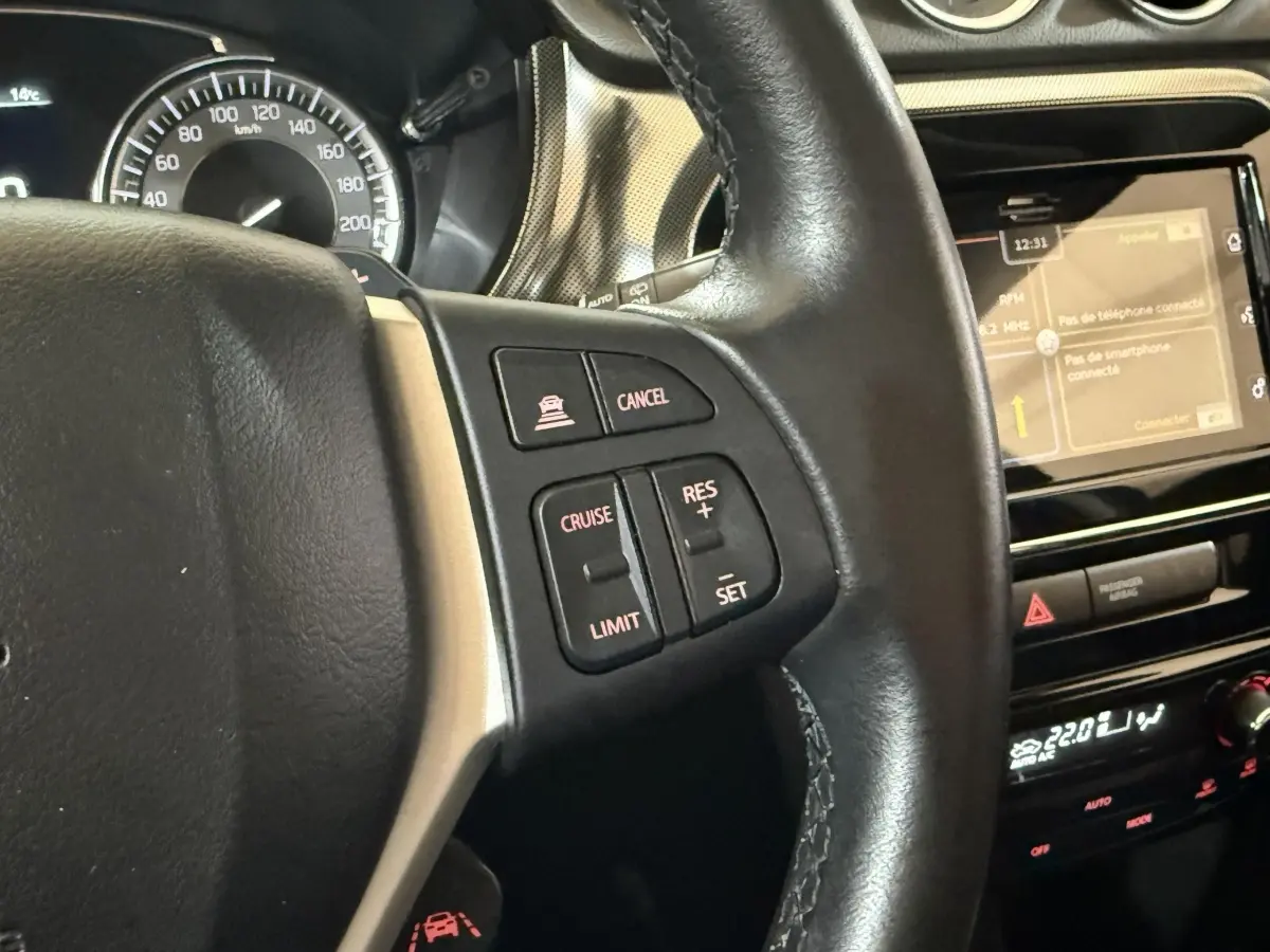 Gros plan sur le volant cuir et alu noir du Suzuki Vitara 2022 avec commandes multifonctions et écran tactile du tableau de bord.