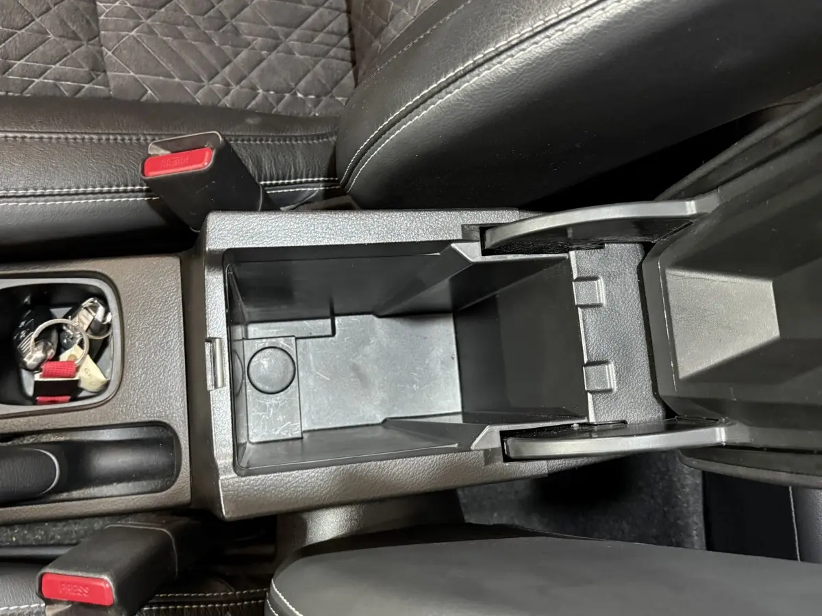 Vue plongeante sur le rangement central ouvert du Suzuki Vitara noir, avec siège et ceinture visibles.