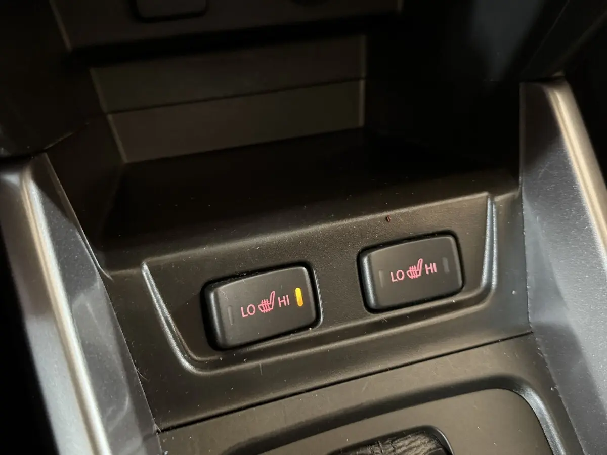 Gros plan sur les boutons de chauffage des sièges avant du Suzuki Vitara noir, avec témoin lumineux allumé à gauche.