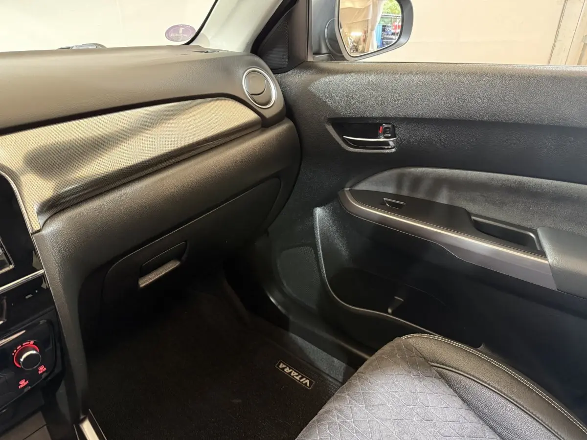 Vue intérieure côté passager du Suzuki Vitara 1.5 Dualjet hybrid noir, avec tableau de bord et porte en plastique noir texturé.