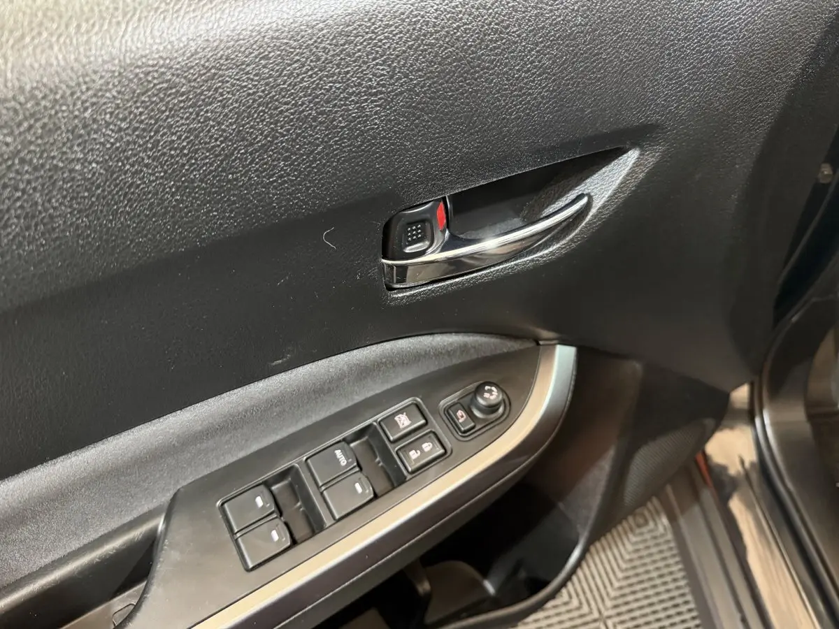 Gros plan sur la porte avant gauche du Suzuki Vitara noir, montrant la poignée chromée et les commandes des vitres électriques.
