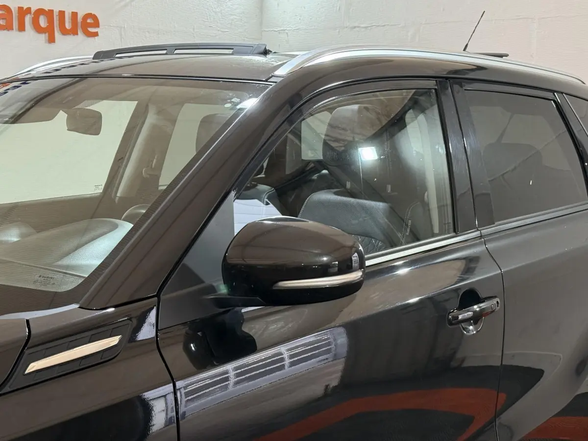 Vue latérale côté gauche d’un Suzuki Vitara noir avec rétroviseur et poignées de porte chromées, intérieur visible.