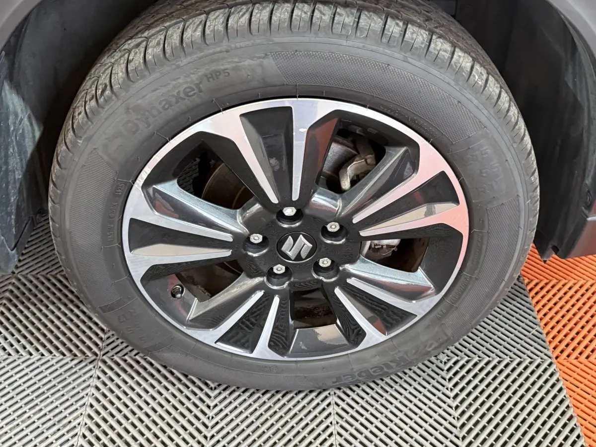 Gros plan sur la roue avant droite du Suzuki Vitara noir, jante alliage bicolore avec logo Suzuki au centre.