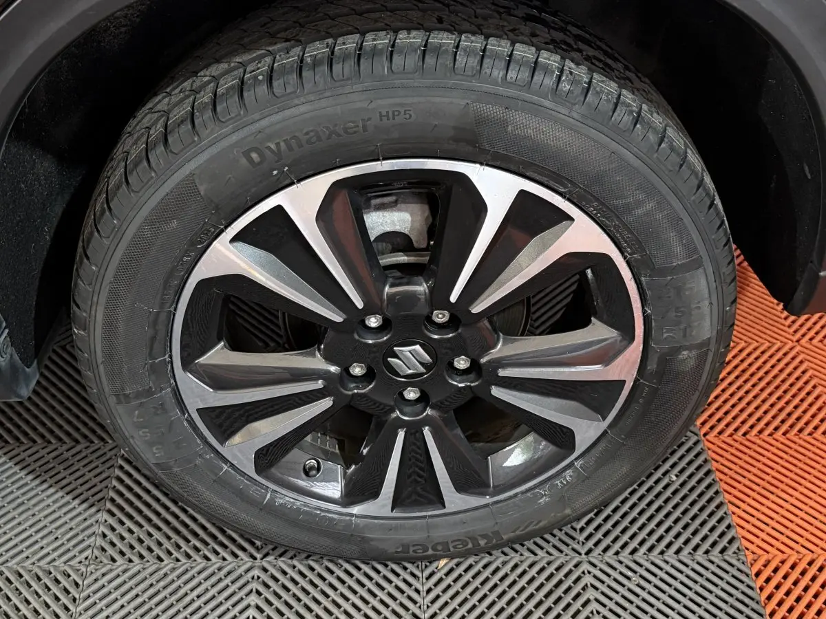 Gros plan sur la roue avant droite du Suzuki Vitara noir, mettant en valeur la jante alliage bicolore au design moderne.