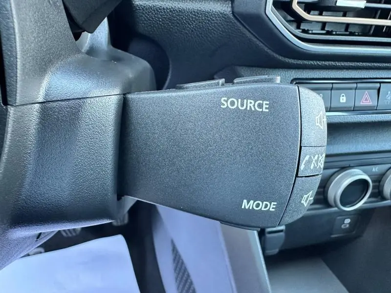 Gros plan sur la commande au volant de la Dacia Sandero beige Safari, avec boutons source et mode visibles.
