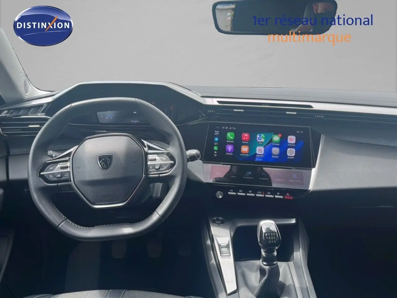Vue intérieure centrée sur le volant Peugeot et la console centrale avec écran tactile et levier de vitesse manuelle.