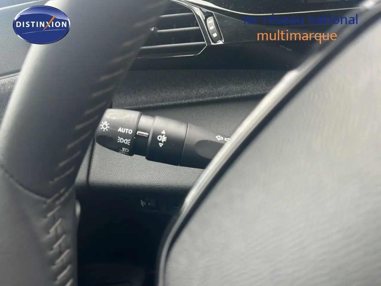 Gros plan sur la commande des phares à gauche du volant dans l’habitacle gris noir d’une Peugeot 308 2024.