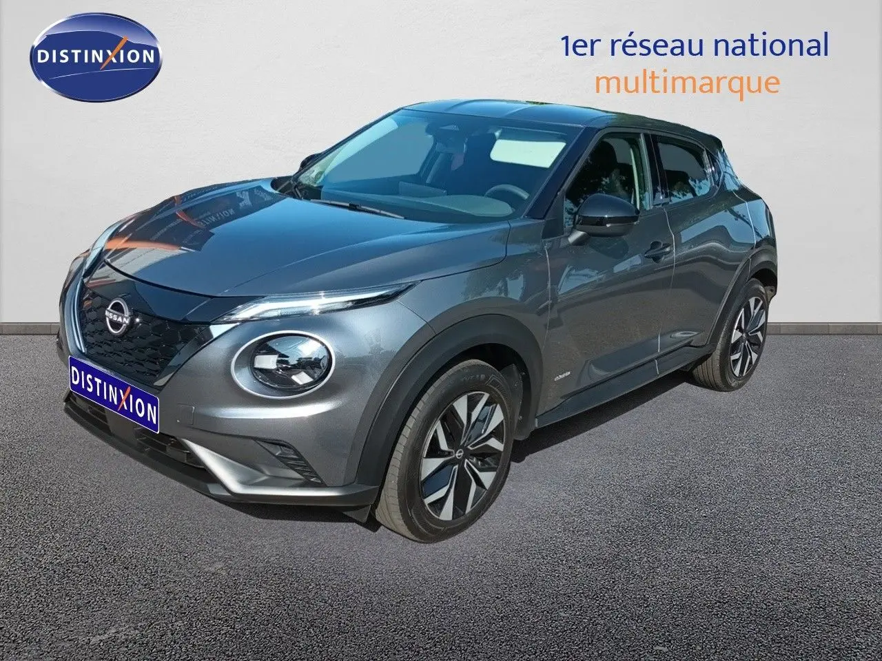 Nissan Juke Hybrid gris squale métal en 3/4 avant droit, avec calandre noire et jantes bicolores distinctives.