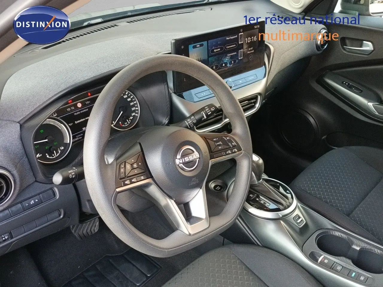 Vue intérieure centrée sur le volant et le tableau de bord d’un Nissan Juke hybride 2025 avec écran tactile et sellerie tissu noire.
