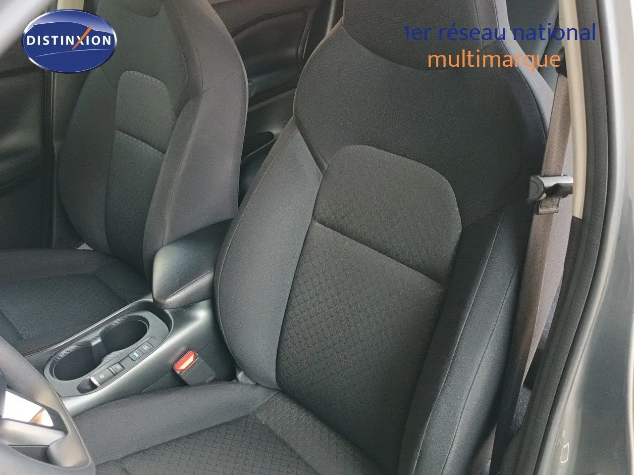 Vue intérieure sur les sièges avant en tissu noir du Nissan Juke Hybrid 2025, avec accoudoir central et ceinture visible.