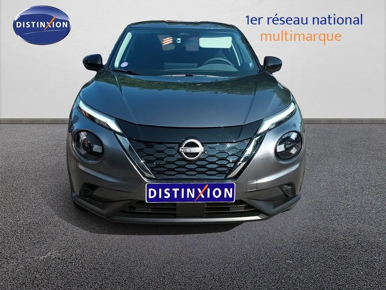 Vue frontale d'un Nissan Juke hybride gris squale métal avec calandre hexagonale et phares ronds distinctifs.