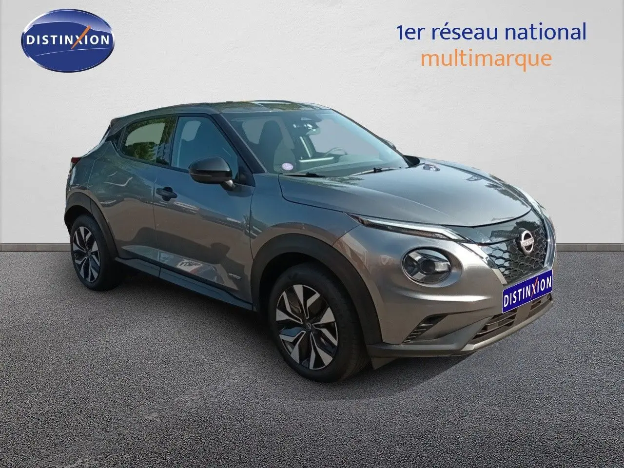 Nissan Juke Hybrid gris squale métal en 3/4 avant droit, avec calandre distinctive et jantes stylisées.