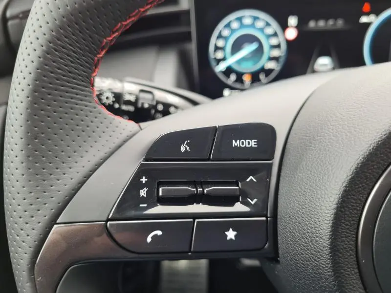 Gros plan sur les commandes audio au volant cuir perforé avec surpiqûres rouges du Hyundai Tucson blanc polaire 2022.