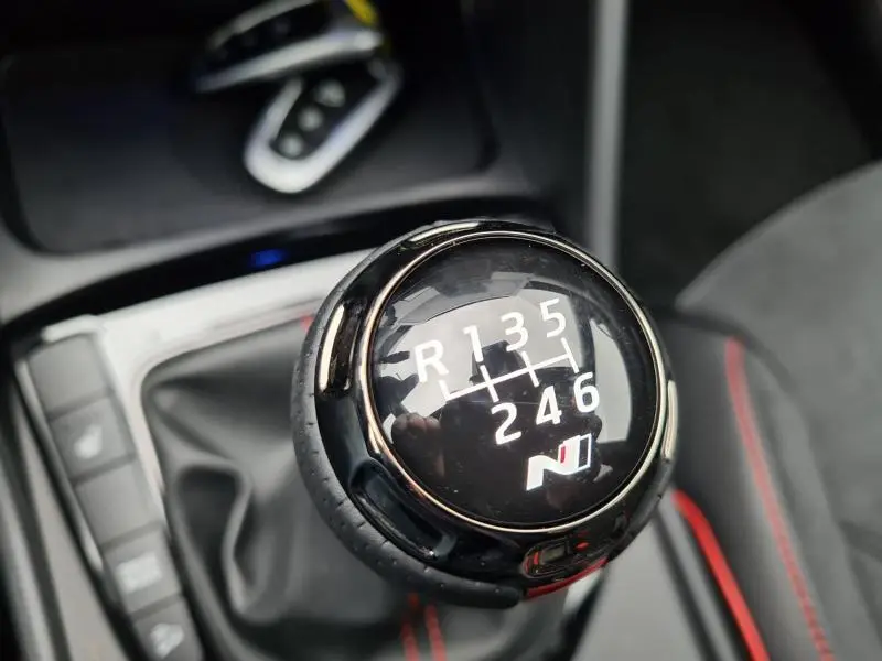 Gros plan sur le levier de vitesses manuel noir avec logo N-Line et coutures rouges dans un Hyundai Tucson blanc polaire toit noir.