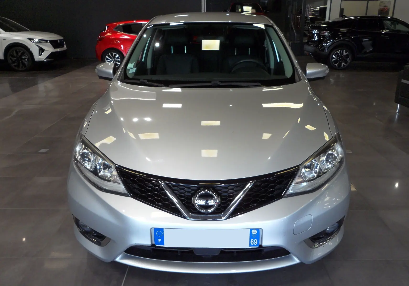 Vue avant d'une Nissan Pulsar gris glacier 2019 avec calandre noire et phares LED en intérieur showroom.