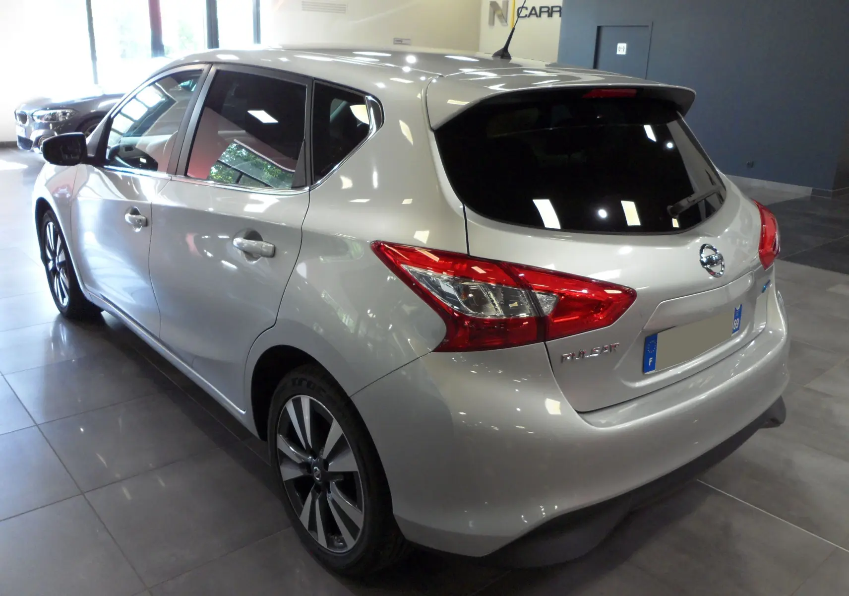 Vue 3/4 arrière droite d'une Nissan Pulsar gris glacier avec jantes alliage et vitres teintées en intérieur showroom.