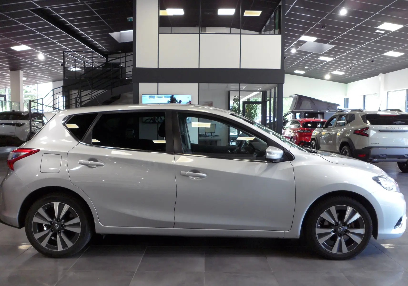 Profil côté gauche d'une Nissan Pulsar gris glacier 2019 en intérieur, soulignant ses jantes alliage et lignes fluides.