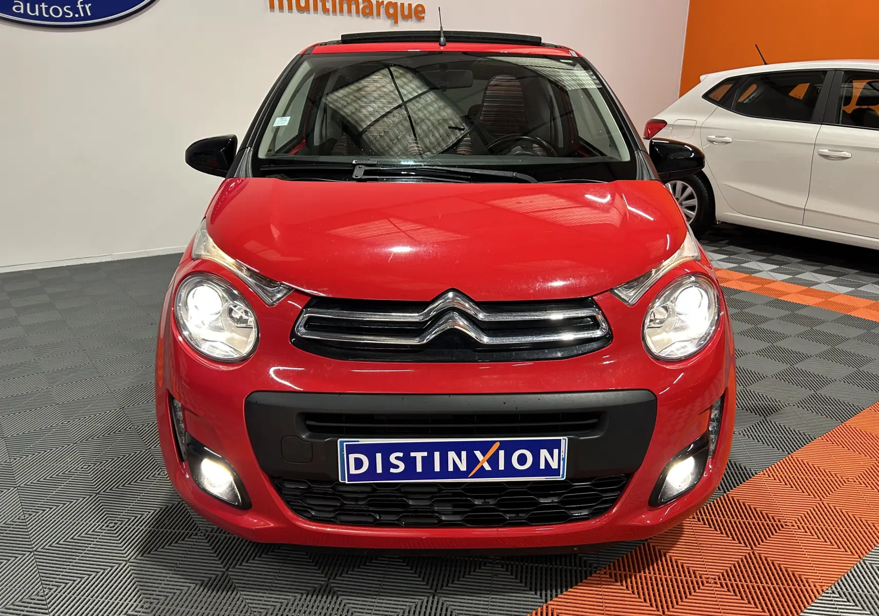 Vue frontale d'une Citroën C1 rouge 2019 avec phares et feux antibrouillard allumés en intérieur showroom.