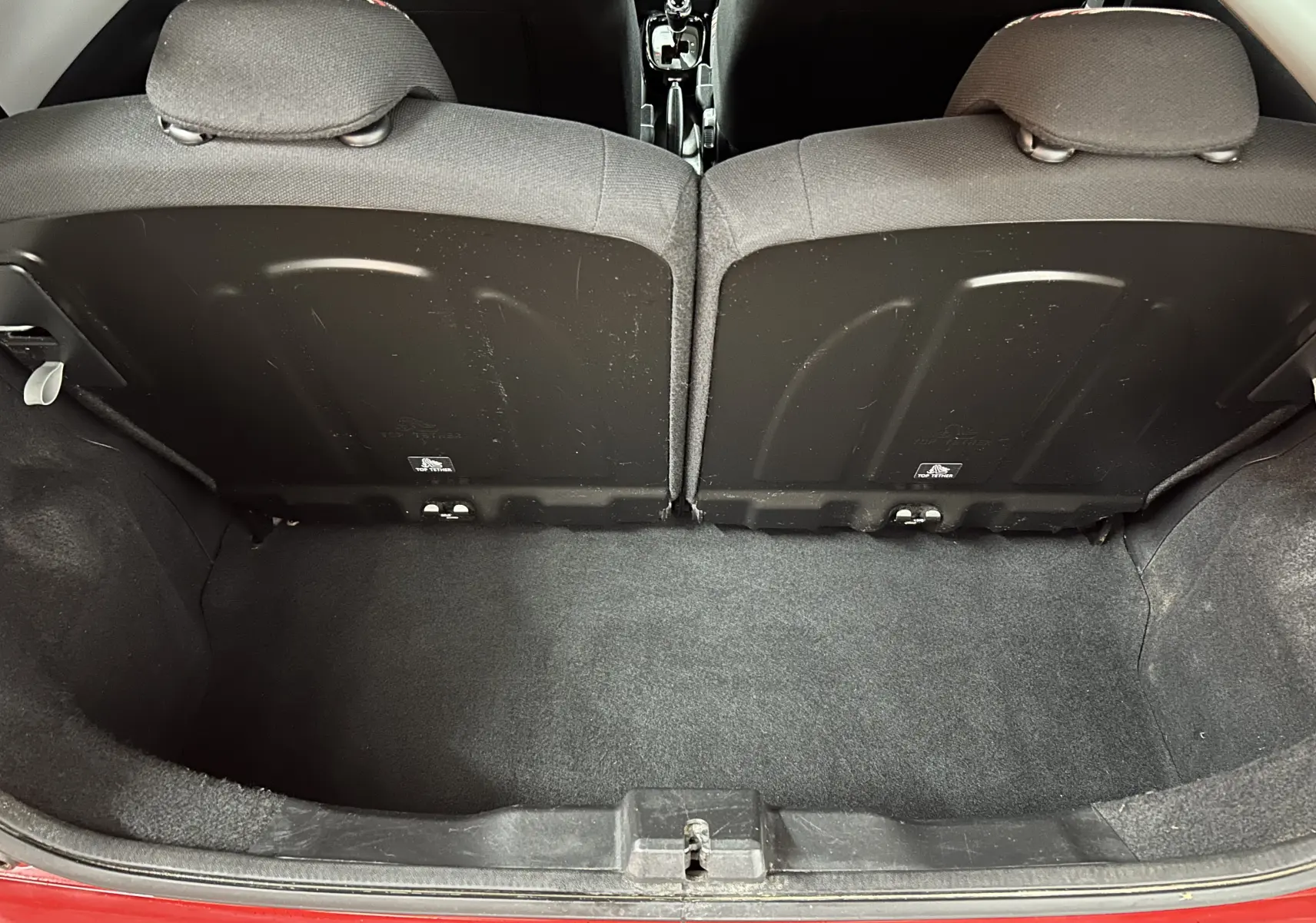 Vue plongeante sur le coffre ouvert d'une Citroën C1 rouge, montrant l'espace de rangement et le dos des sièges arrière.