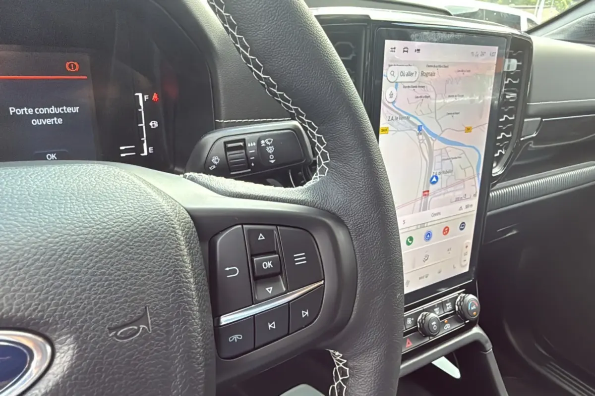 Intérieur du Ford Ranger 2025 noir agate, vue rapprochée du volant avec commandes et écran tactile vertical affichant la navigation.