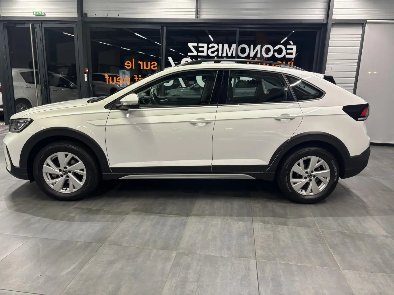 Vue de profil côté gauche d’un Volkswagen Taigo blanc, avec jantes alliage et protections noires sur les bas de caisse.