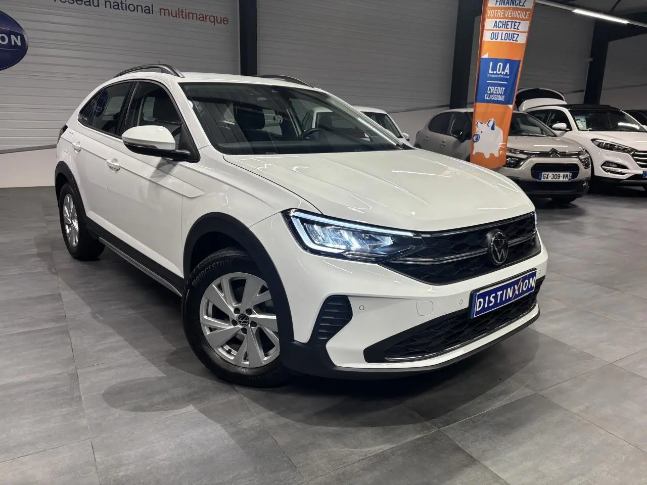 Volkswagen Taigo blanc en 3/4 avant droit, avec jantes alliage et phares LED allumés en intérieur showroom.