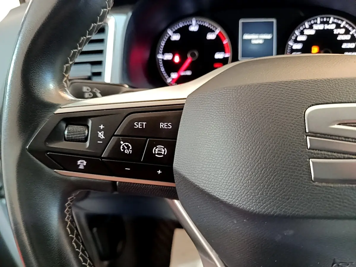 Gros plan sur le volant cuir et alu côté gauche du SEAT Ateca gris clair avec commandes multifonctions et tableau de bord lumineux.