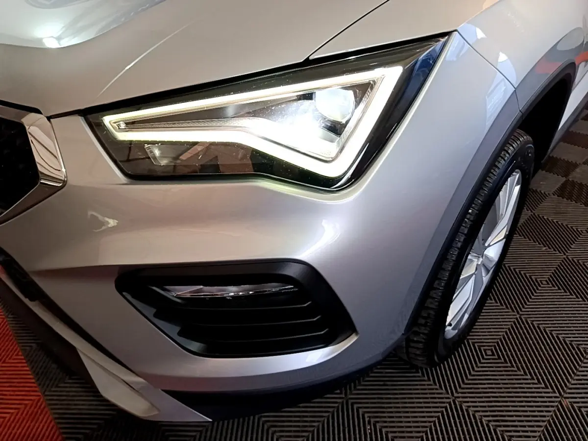 Gros plan sur le phare avant droit allumé d’un SEAT Ateca gris clair, avec partie de la roue visible.
